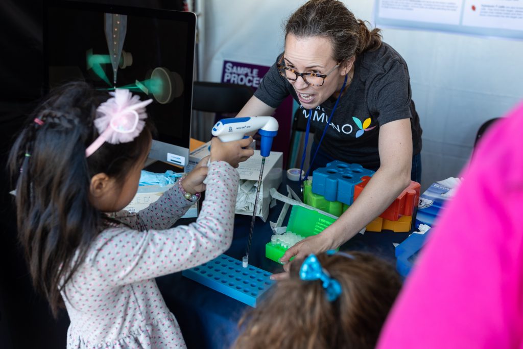 A scientist helps a girl try pipetting.