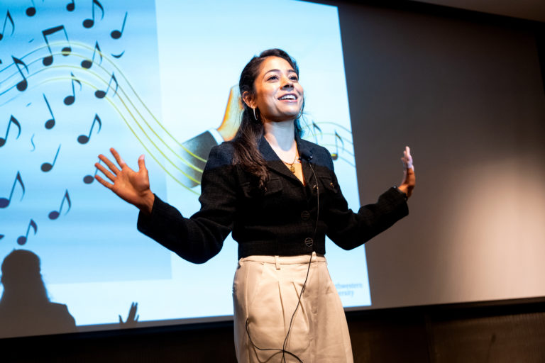 Post doc grade slam participant smiling and holding up hands while explaining research in 3 minutes.